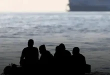 Four people silhouetted on a small boat at sea with a large ship in the background
